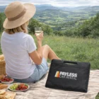 Woman picnics with wine and Comfy Stadium Cushions, Payless Car Rental bag in foreground.