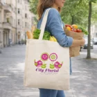 Woman carries groceries in Aylesbury Branded Cotton Totes on city street with flowers and birds.