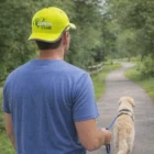 Man in blue shirt and Capri Hi-Vis Cap walking a dog on a park path.