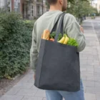 Person carrying a gray Mokko Cotton Tote Bag filled with bread, bananas, and vegetables.