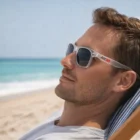 Man in Soho Translucent Sunglasses relaxes on a beach chair by the ocean on a sunny day.