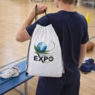 Person in sportswear holding a Solana Drawstring Backpack with CleanEnviro EXPO 2016 logo at gym.