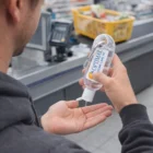 Applying Alia Carabiner Hand Sanitiser at checkout with a shopping basket behind.