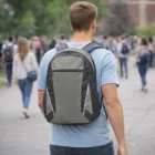 Man with a gray Doxa Backpacks walking outdoors among a crowd.