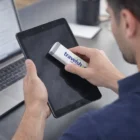 A person uses Valsum Screen Cleaners to wipe a tablet screen at their desk.