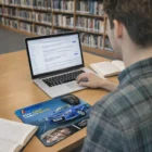 Man working on laptop in library with Moogle 4-In-1 Mouse Mats and open books on the table.
