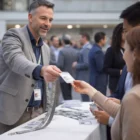 Man handing Kallis Premium Lanyards to attendees at a conference registration table.