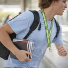 Person with backpack and books, wearing a green Stitchlasso Woven Lanyard, walking indoors.