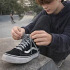 Teen tying Personalised Woven Shoe Laces on black Vans at skatepark in dark clothes.