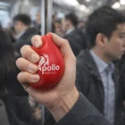 Hand squeezing a Blood Drop Stress Ball with Apollo Hospitals branding on a crowded subway.