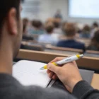 Person taking notes with a Nikko Pens White Barrel in a lecture hall, viewed from behind.