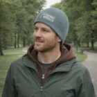 Man in green jacket wears Idaho Promo Garter Knit Beanie Cap on park path amid Idaho greenery.