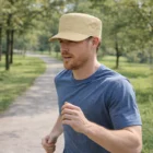 Man jogging on a tree-lined park path wearing a Military Style Cap and blue shirt.