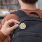 Person pins a Lapiz Lapel Pins Round Small to a black backpack featuring a yellow cartoon.