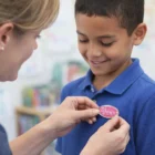 An adult pins a Lapiz Lapel Pins Oval on a smiling boy’s blue shirt.