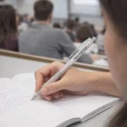 A person writes in a notebook with a Nyla Ball Pen in a classroom.