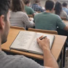 Student taking notes in a Damian Medium Branded Notebook during class.