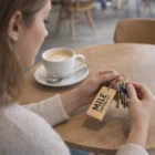 Woman holding keys with Rectangle Wooden Keyrings at a café table with coffee.