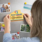 Hands placing a House Fridge Magnet With Bulk Printing among family photos—great for bulk orders.