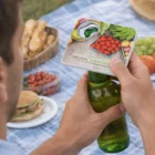 Man opening a drink with a Handy Square Bottle Opener at an outdoor picnic table.