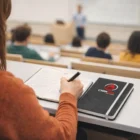A student takes notes in a lecture hall with a Meredith Promo Notebooks Two Tone on the desk.