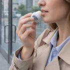 Woman applying Sahara Lip Balm Balls outdoors, wearing a beige coat and light blue shirt.