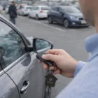 Person unlocking a parked car with a Gunmetal House Keyring remote in a parking lot.