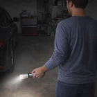 Person in a garage shining the Torch Nexus flashlight toward a parked car.
