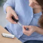 Woman trims nails with Personalised Compact Plastic Scissors; kit case is on the table.