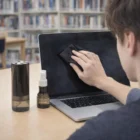 Person cleaning a laptop screen with Flawless Screen Cleaning Kits; supplies on the table.