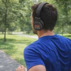 Man in blue shirt jogging in park, wearing Hercules Printed Logo Bluetooth Headphones.