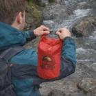 Person holds a Stay Dry Custom Printed Travel Bag near a rocky stream outdoors.