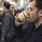 Man enjoys coffee in a Zylin Glass Cup while riding a busy train.