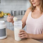 Woman adds protein powder to a 400Ml Zeus Fitness Shakers Logo Decorated bottle in the kitchen.