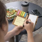 Person writing in a notepad with Marengo Mini Note Wallets, salad, and coffee outdoors.