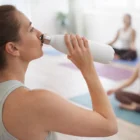 Woman drinking from a Jovian Vacuum Bottles One Litre in a yoga studio with others behind her.