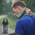 Man cools his neck outdoors with Razzle Premium Cooling Towels; water bottle by his side.