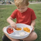 Young boy enjoys snacks from Bailey BPA Free Snack Tray while sitting on grass outside.
