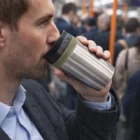 Man drinking from an Aspen 400Ml Stainless Steel Cup in a busy outdoor scene.