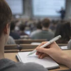A student takes notes with a Lamy Safari Plastic Pen in a crowded lecture hall, focused on writing.