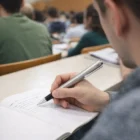 Student writes notes with Lamy Studio Elegant Ball Pens during class, surrounded by classmates.