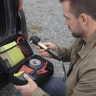 A man holds a flashlight by an open car kit with Emergency Vehicle Tools inside.