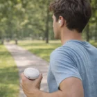 Man in gray shirt walks in park holding Blitz Bluetooth Earbuds case.