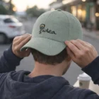 A person adjusts a gray Tank Caps hat with an idea and light bulb logo, seen from behind.