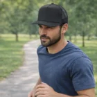 Man jogging in a blue shirt and black George Flat Peak Mesh Cap along a tree-lined park path.