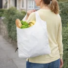 Person carrying Compact Folding Shopper Bag with groceries: bread, lettuce, and bananas.