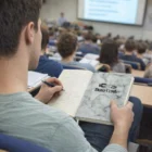 Student taking notes in a Soft Marble Look Notebook labeled "Data Center" in lecture hall.