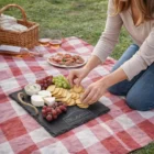 Woman arranges cheese and crackers on Elana Serving Boards with fruit and wine outdoors.