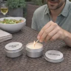 Man lighting Outdoor Citronella Candles Bulk in a tin labeled Your Logo Here on a table.