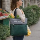 A woman walks on a city sidewalk carrying lemons in a Turin Tote Bag.